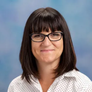 Erin DiCaprio is wearing a white, collared button down and has glasses and brown hair. 