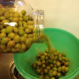 Green olives poured from glass jar into a green colander.