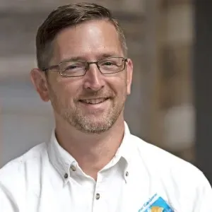 headshot of a man with light brown hair and glasses wearing a white collared shirt with the UC Master Gardener logo
