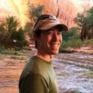 A man wearing a hat, standing in front of a river