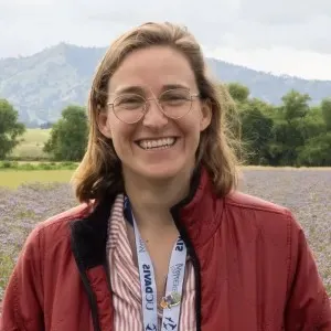 A woman with short light hair wearing glasses and a red jacket and standing outdoors