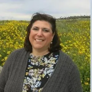 woman with short dark brown hair standing in a field of yellow flowers
