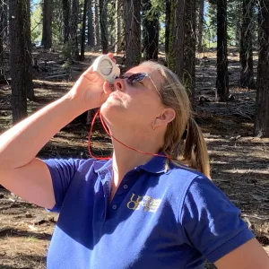 Woman holding a clinometer up to her eye.