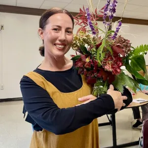 brunette woman holding a vase of assorted flowers and foliage