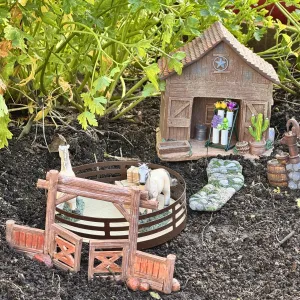 miniature figurines of a barn, horses and a corral with a background of plants