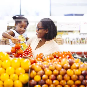 A mother and holds her young daughter in her arms while selecting apples in the produce section of a grocery store.