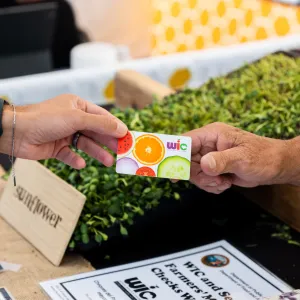 Image of a WIC card being handed between 2 people at a farmers market.