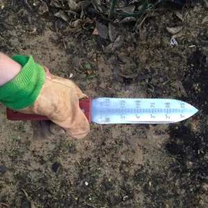 a garden-gloved hand gripping a hori hori knife