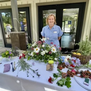 a woman stands behind a table filled with pieces of flowers and plants