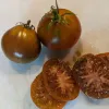 Two whole Japanese Black Trifele tomatoes beside a sliced tomato, showcasing their rich brownish-red color and seeds within.
