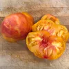 A ripe German Bi-Color tomato, cut in half, revealing its bright yellow and orange inner flesh with red accents, resting on a wooden cutting board.