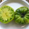 Two tomatoes on a white plate: one sliced, showing light green flesh, and one whole, deep green, round tomato.