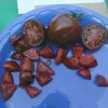 A blue plate with a whole Black Zebra tomato, two halved tomatoes, and several wedge-shaped pieces, all showcasing a dark reddish-brown color with a red interior.