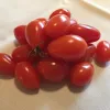 A cluster of bright red cherry tomatoes on a light fabric surface, featuring smooth skins and one tomato with a green stem attached.
