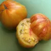 Two ripe, striped tomatoes on a green cutting board; one is whole, and the other is cut in half, showing its juicy interior.
