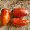 Three elongated, glossy red tomatoes with orange and yellow streaks arranged on a speckled granite countertop.