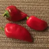 Three red peppers of varying shapes sit on a textured brown surface.