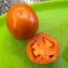 A whole orange Glory of Moldova tomato next to a halved tomato on a green cutting board, showing its juicy interior and seeds.