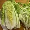 A halved napa cabbage on a wooden cutting board, with thin strips of cabbage beside it.