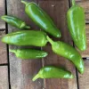 A variety of fresh green peppers in different sizes and shapes arranged on a wooden table.