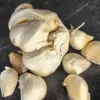 A cluster of garlic bulbs on a dark surface, featuring a larger bulb with exposed cloves and smaller individual cloves scattered around.