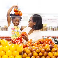 A child holds a cluster of tomatoes over her head as she smiles at a grocery store