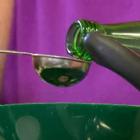 Hands pouring a liquid from a bottle into a small measuring spoon